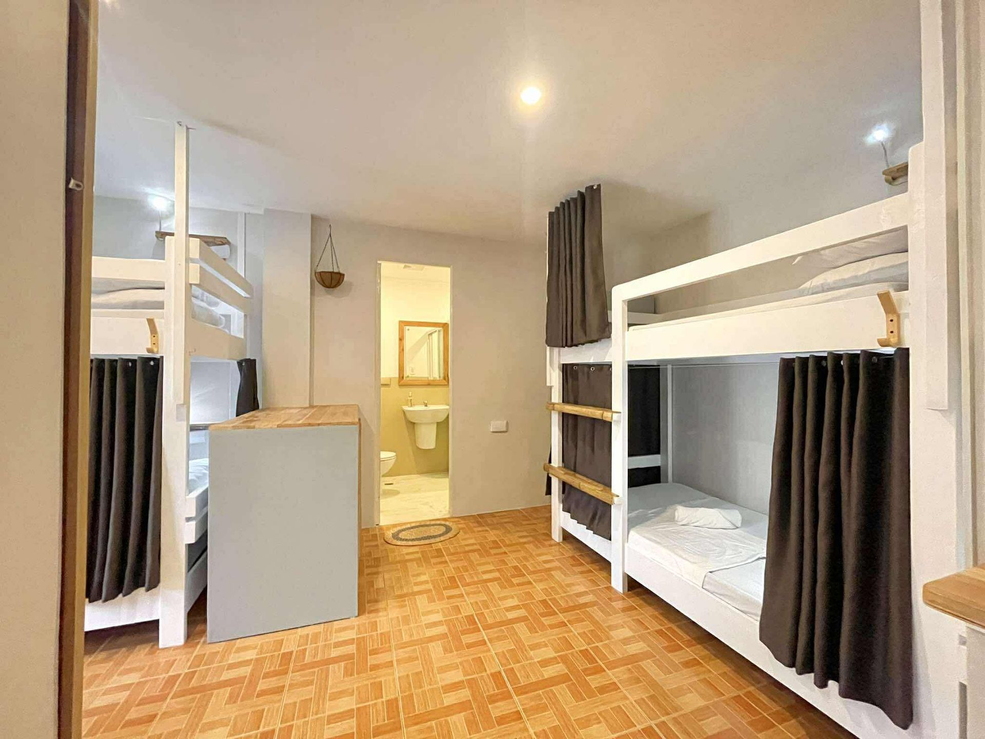 Hostel dorm room with white bunk beds, brown curtains, and a tiled floor. Bathroom in background.