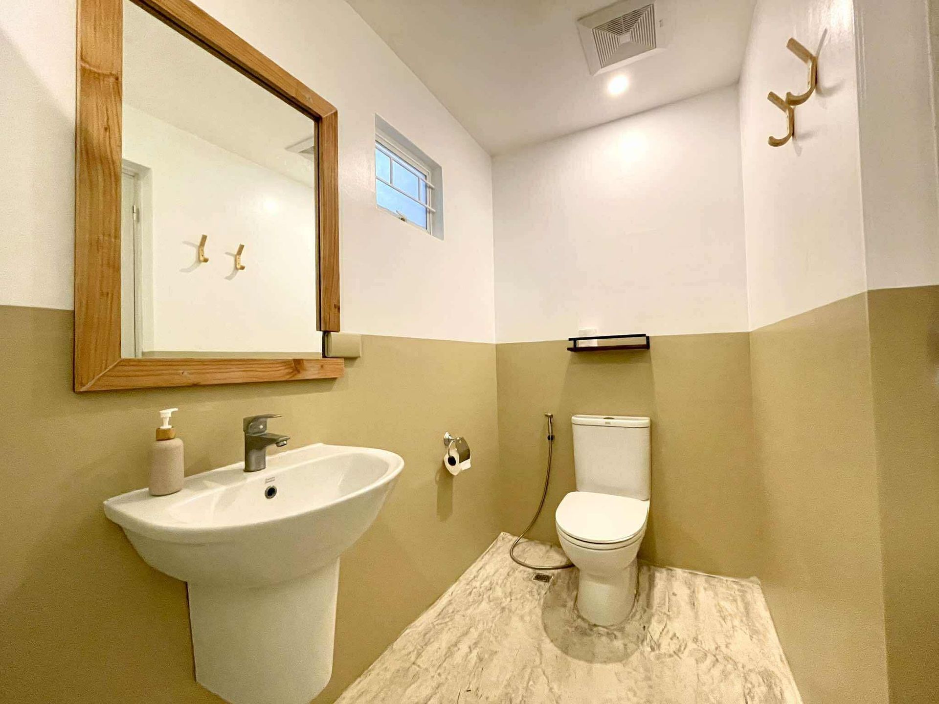Bathroom with pedestal sink, toilet, and mirror with wooden frame. Two-tone beige and white walls.