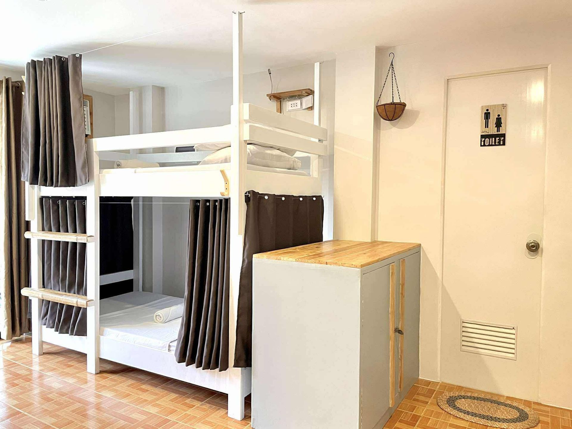 Bunk beds with curtains in a hostel room, next to a cabinet and a bathroom door.