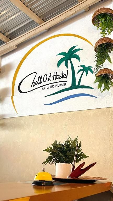 Sign for Chill Out Hostel with palm trees, blue water, and hanging plants.
