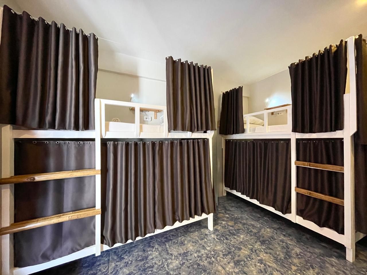 Bunk beds with brown curtains in a hostel room; white frames, blue floor.