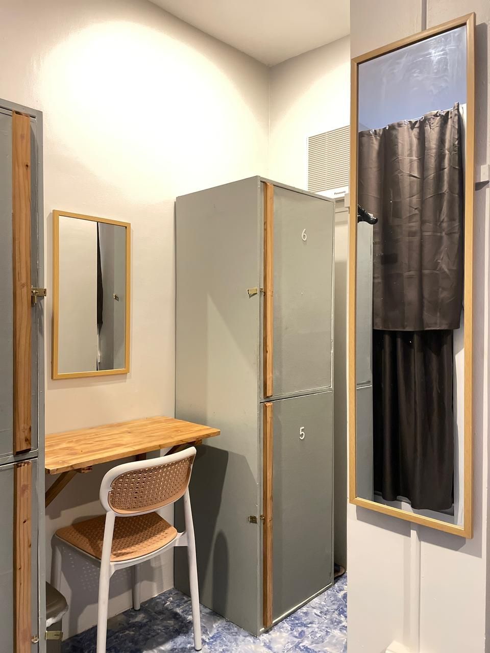 A dressing room with three gray lockers, a chair, and mirrors. A brown curtain hangs in the open dressing room.