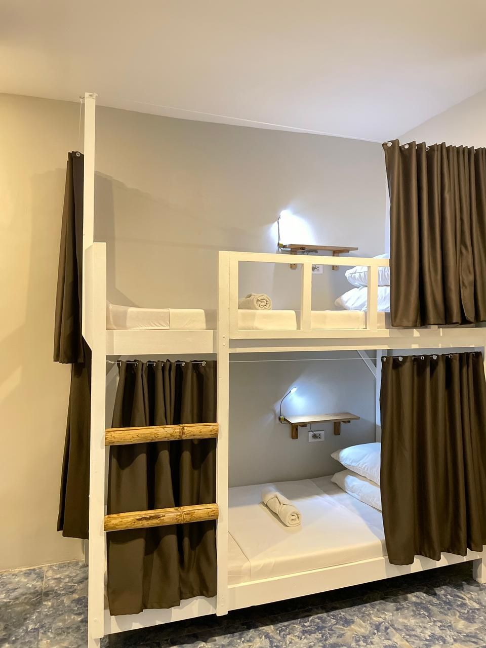 Bunk beds in a room with white walls, brown curtains, and a wooden ladder.  White sheets and pillows are visible.