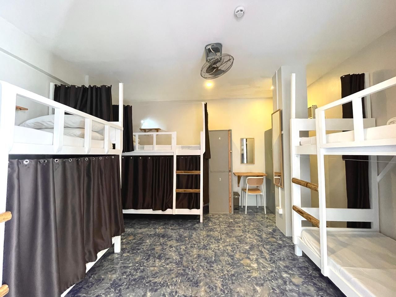 A hostel room with multiple bunk beds, brown curtains, and a desk.