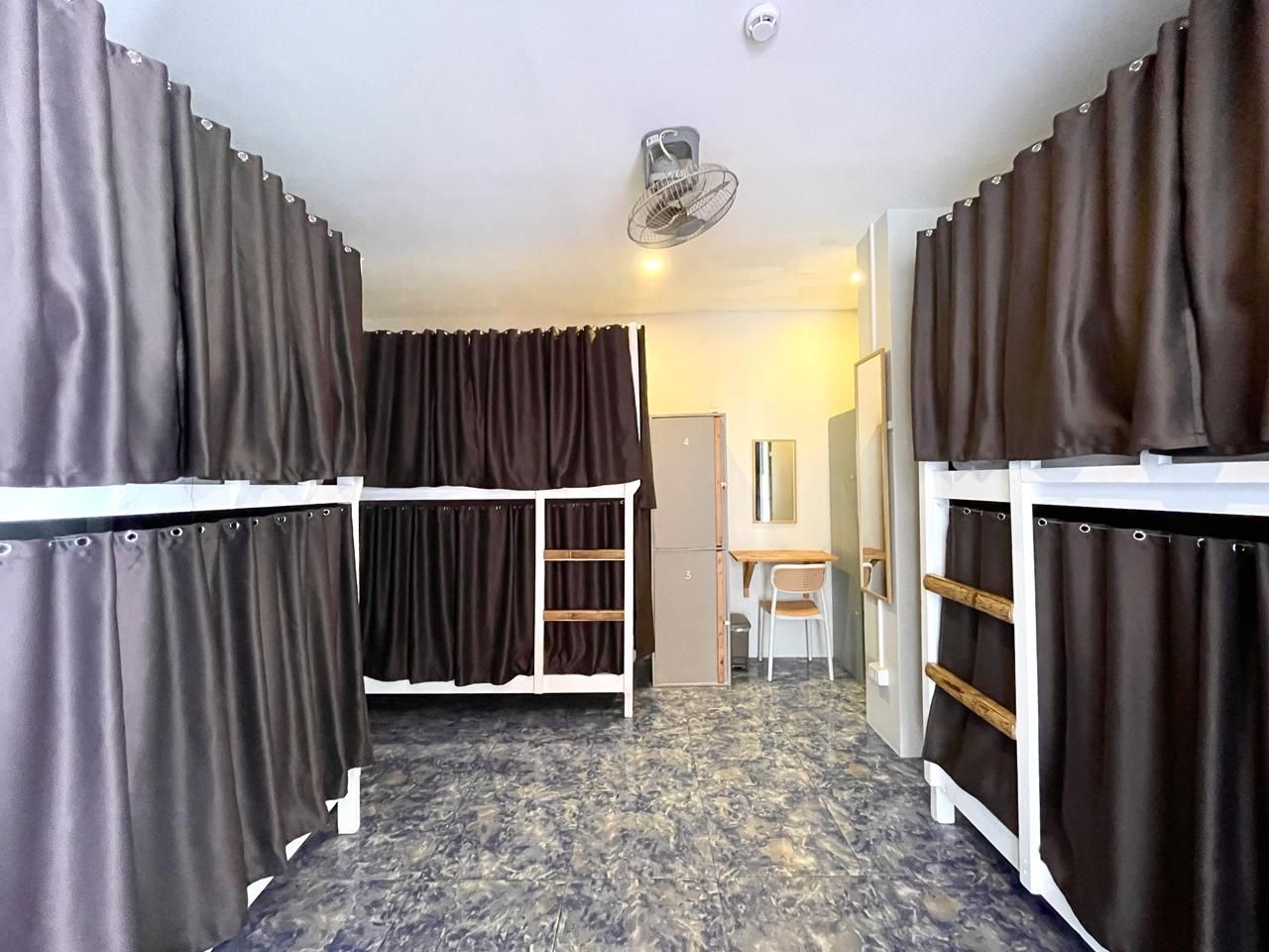 Dorm room with bunk beds, brown curtains, blue tile floor, desk, and ceiling fan.