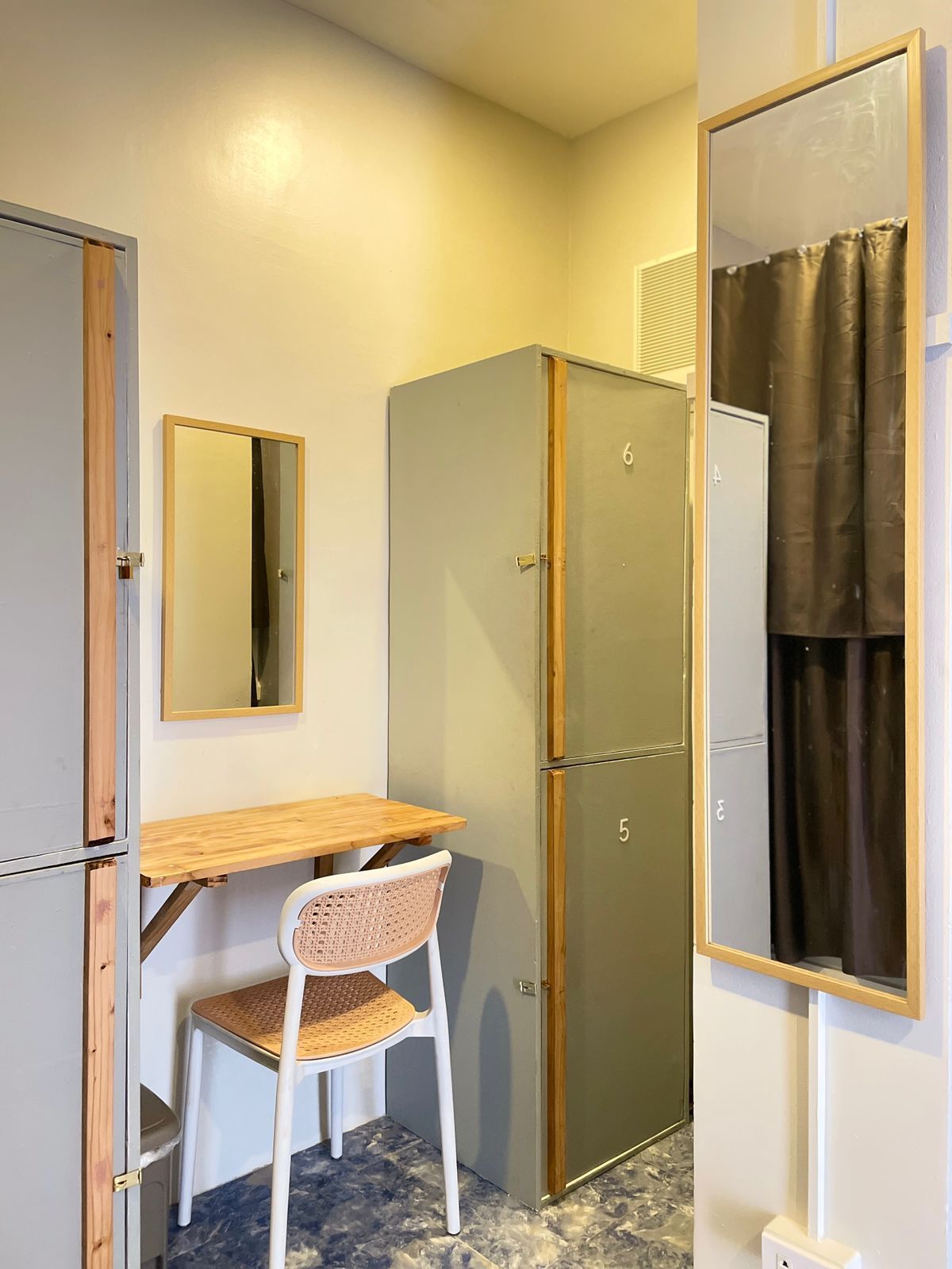 Locker room with gray lockers, a folding desk, a chair, and a full-length mirror.