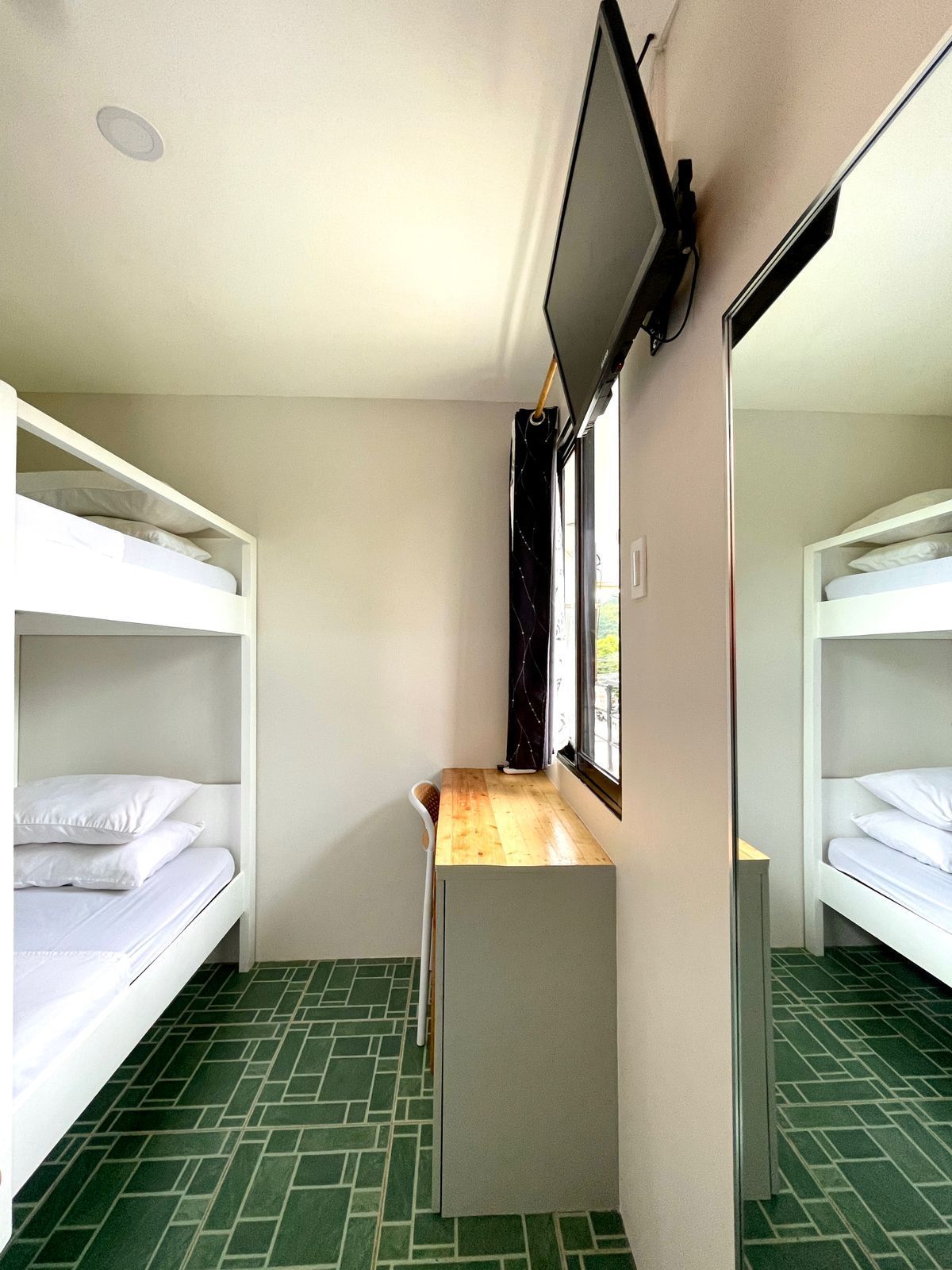 Bedroom with two bunk beds, a desk, and a TV; green tiled floor, white walls.