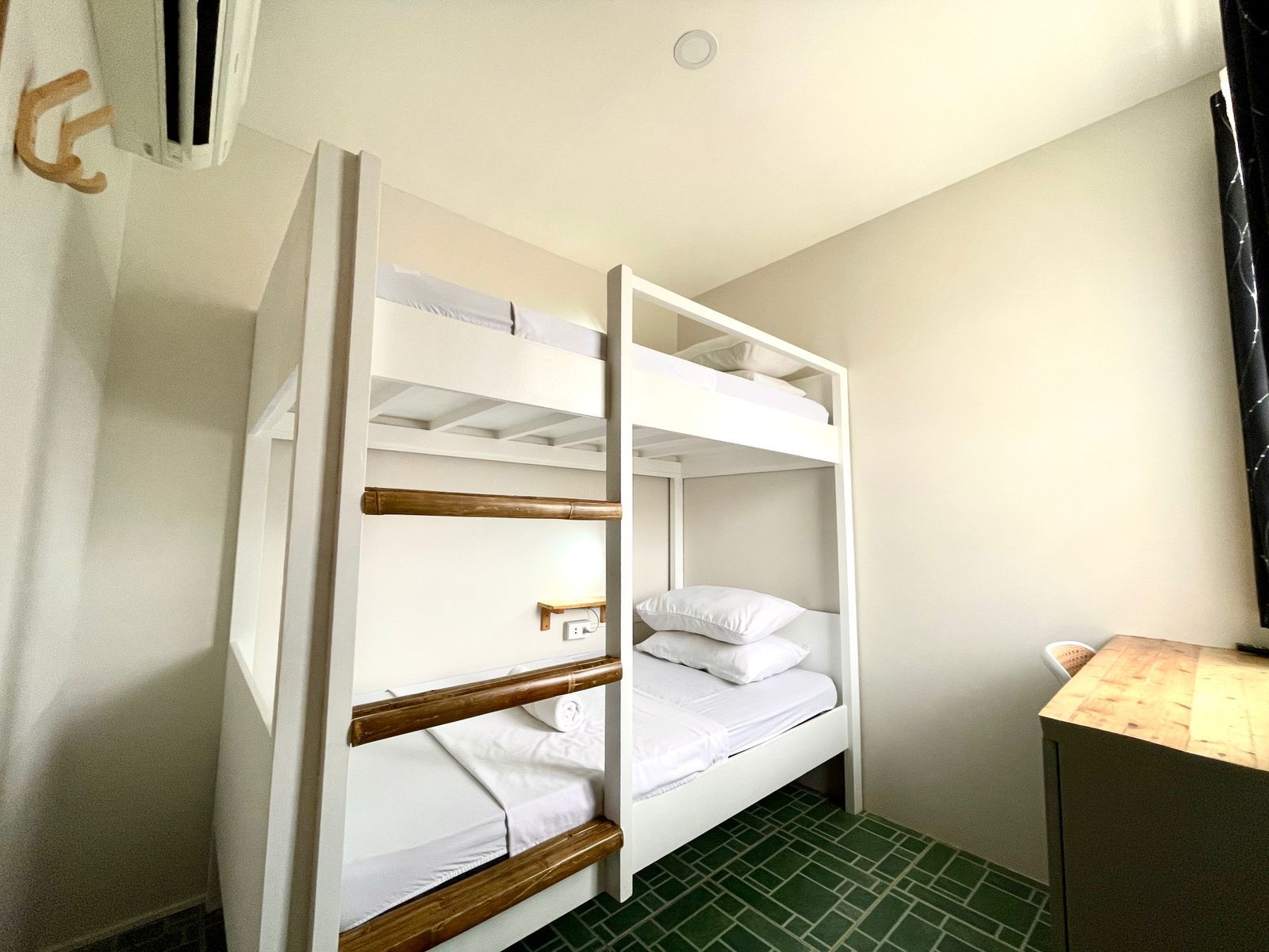 White bunk beds in a room with green flooring and a wooden side table.