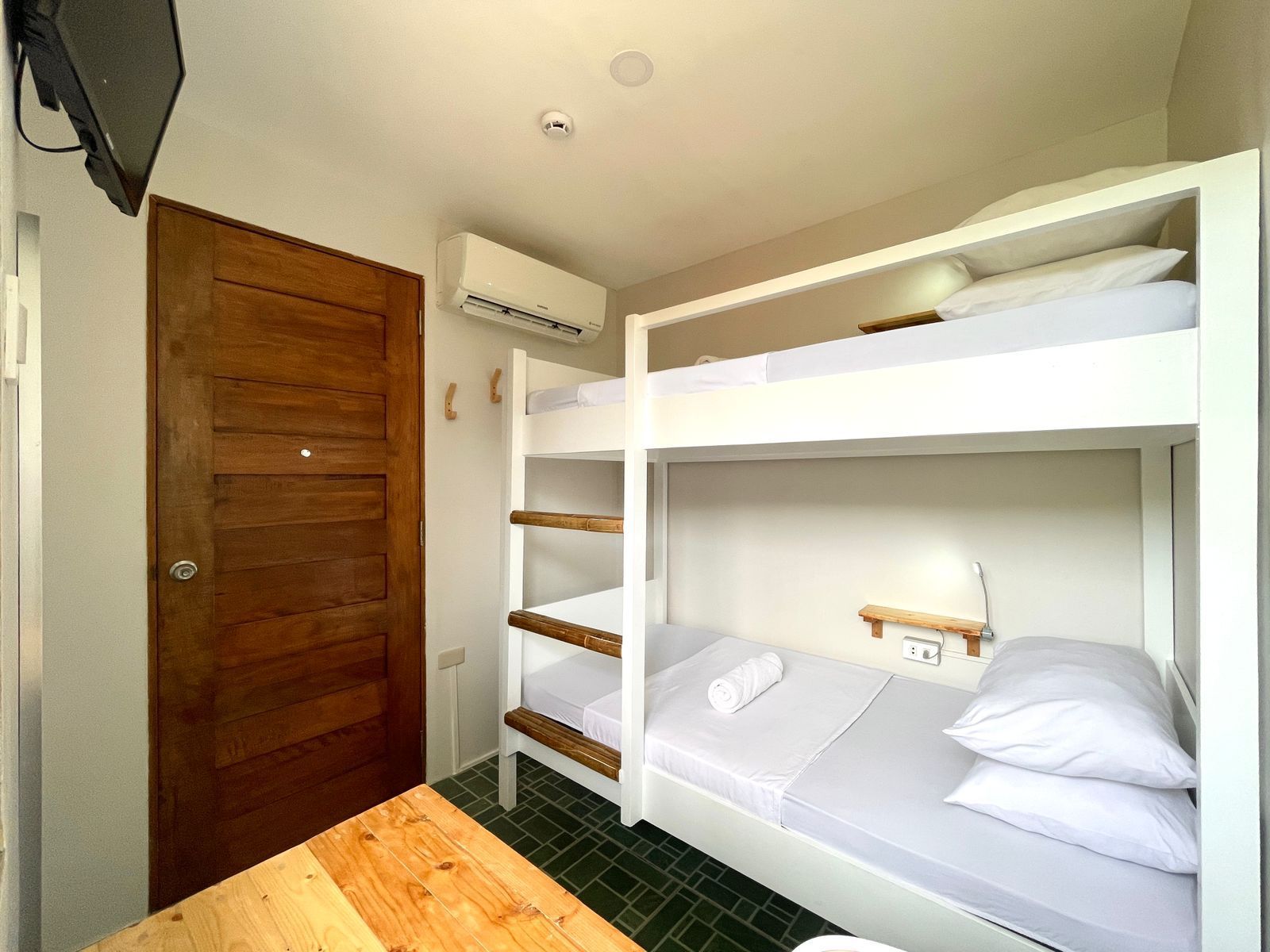Bunk beds in a small room with a wooden door, AC unit, and a small table.