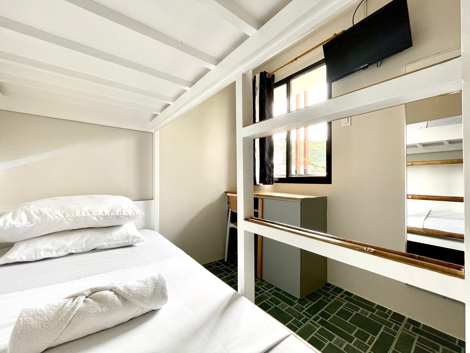 Bunk beds in a bright room with a small window, TV, and desk. White linens and towels.