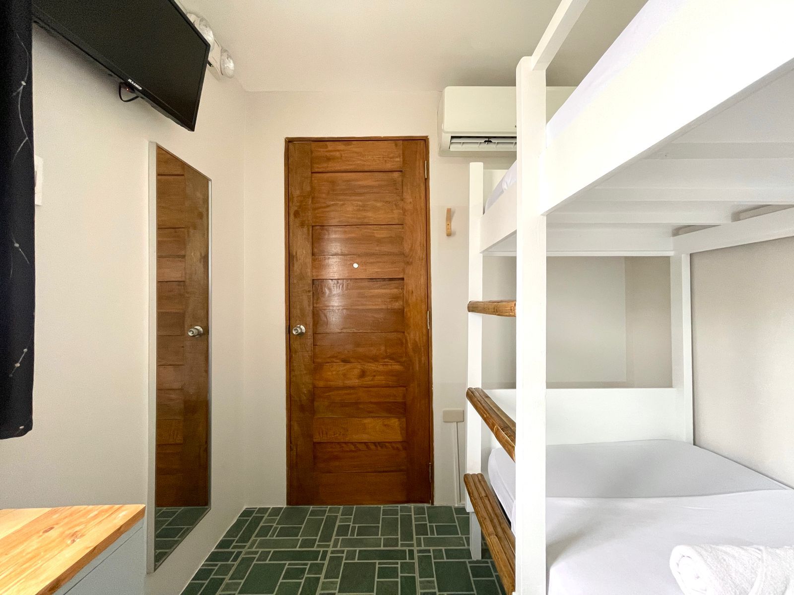 Bunk beds, door, and mirror in a small room with a TV. Green tiled floor.