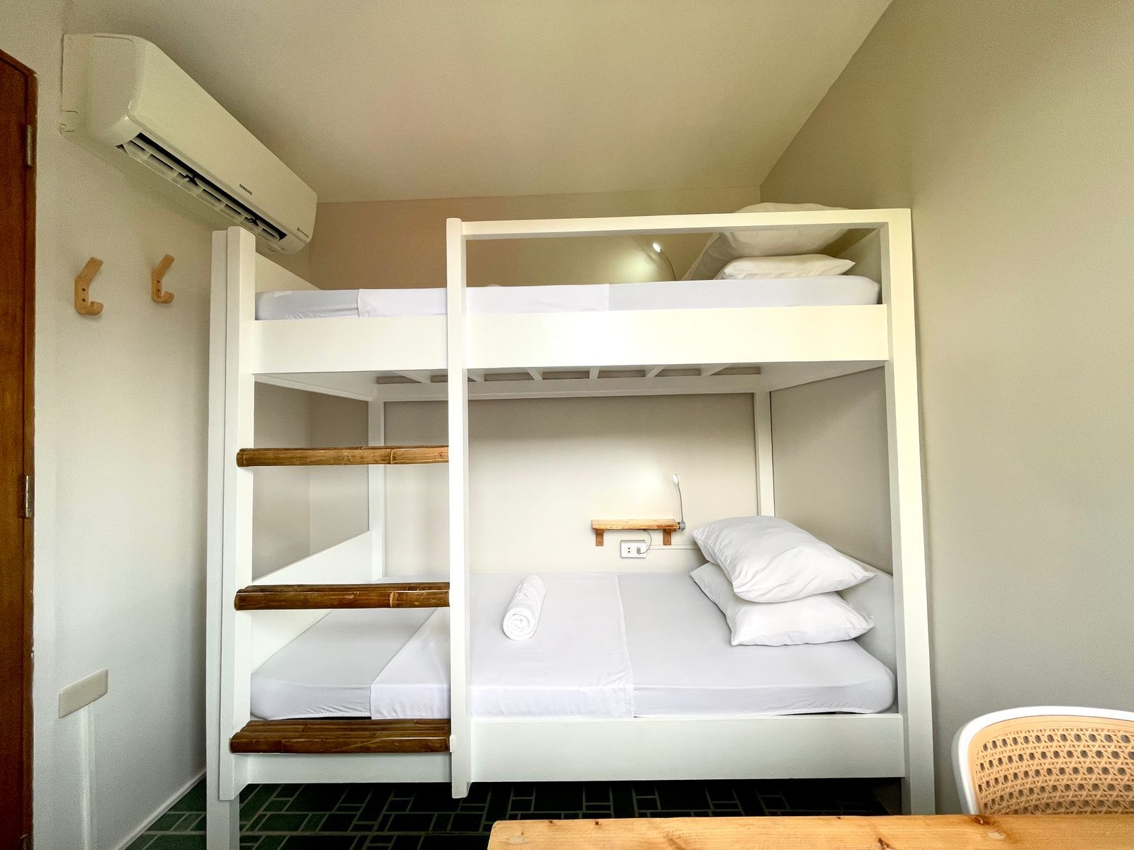 White bunk beds in a room with air conditioning, wooden steps and side rails, white bedding.