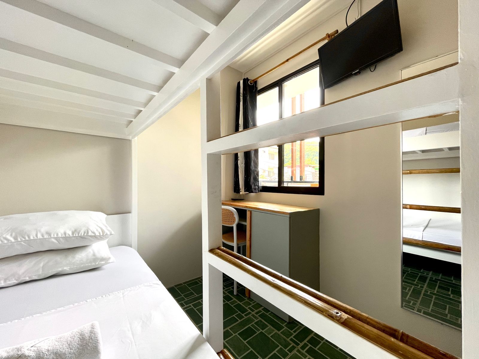 Bunk bed in a brightly lit room with a small desk and television, white and green color scheme.