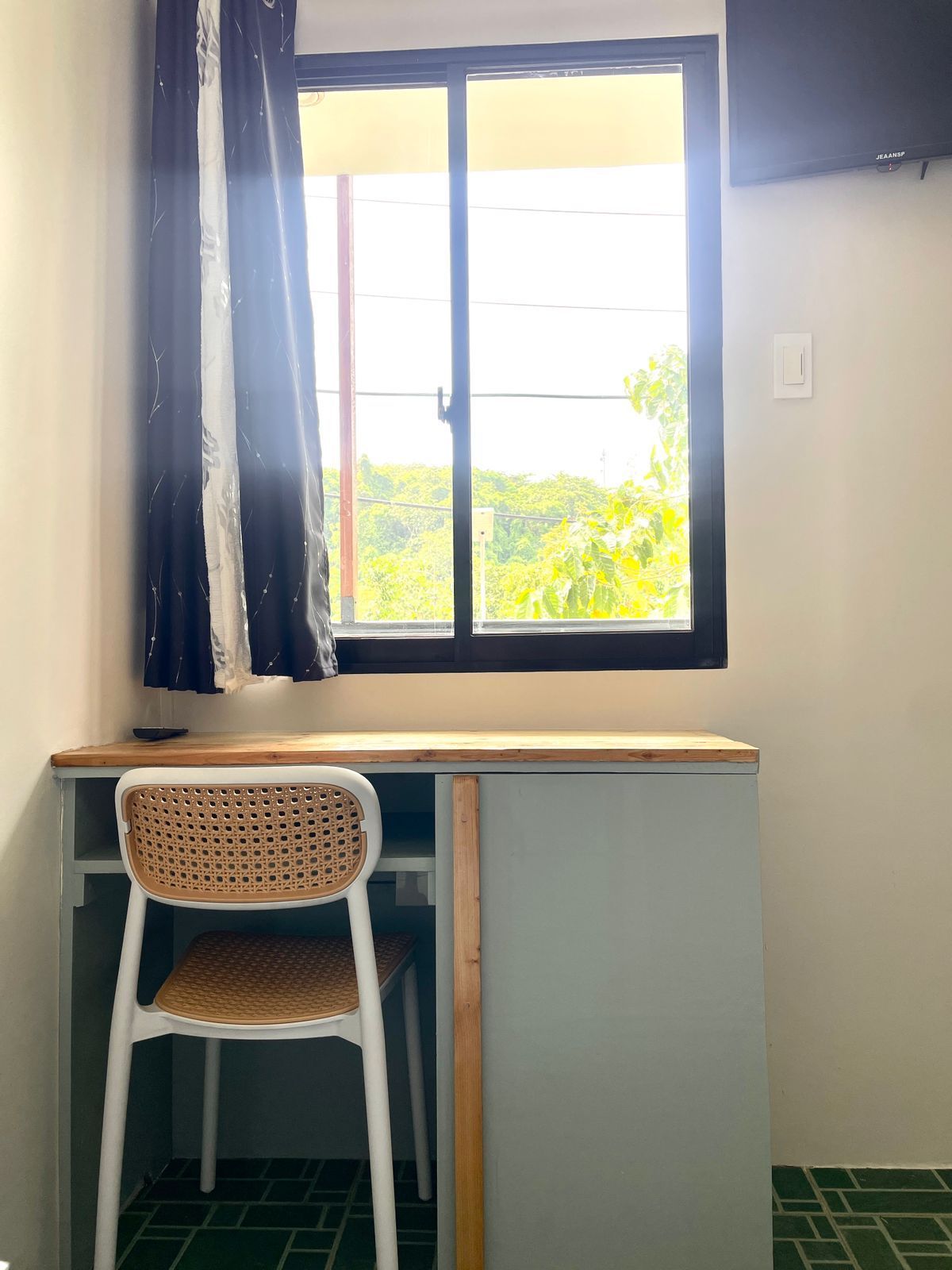 Desk with wicker chair by a window with sheer curtains.