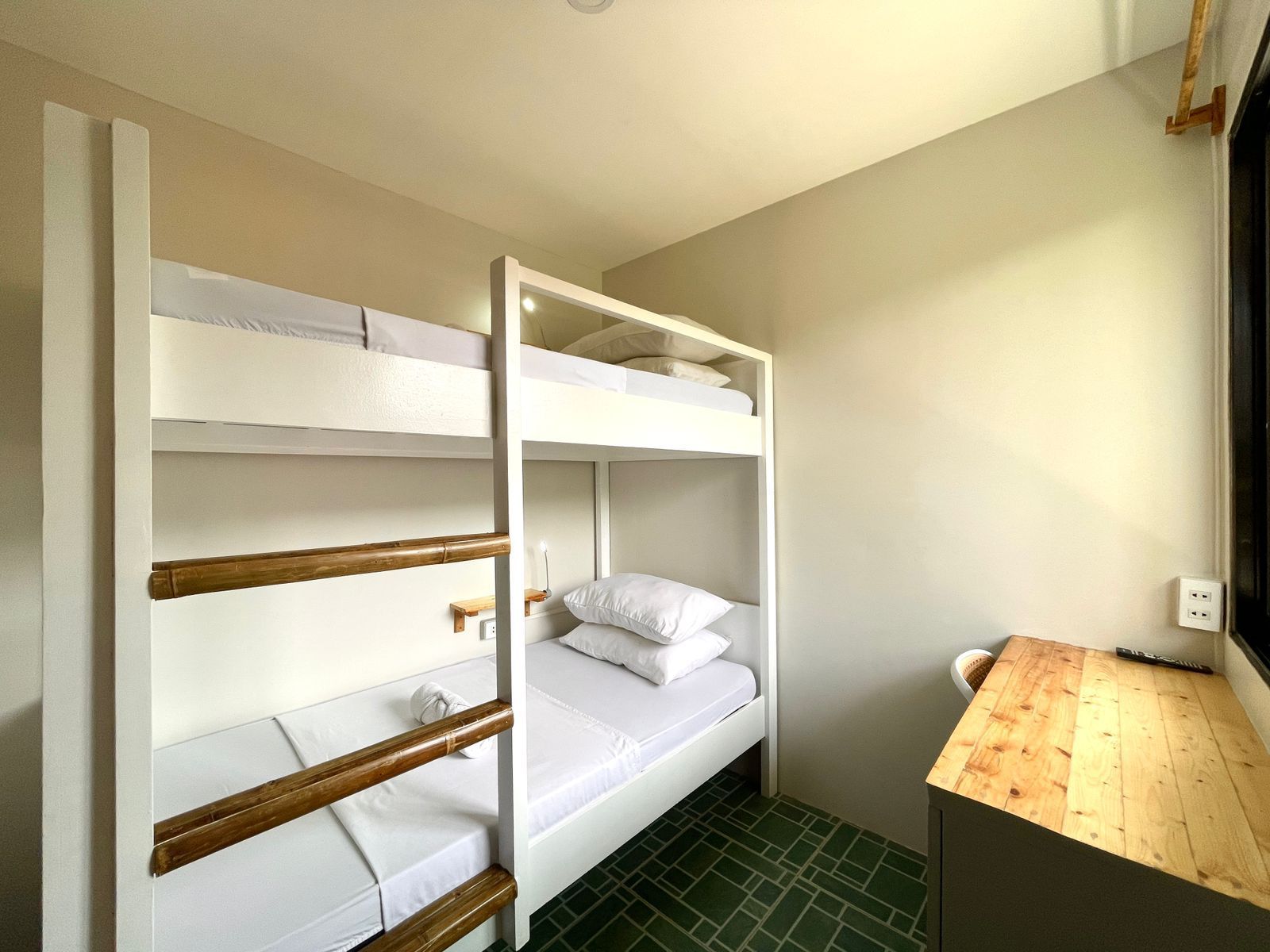 Bunk beds in a small room with light-colored walls and a wooden desk. Green tiled floor.