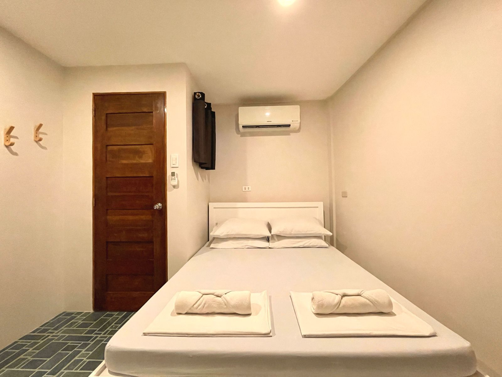 Small bedroom with a bed, TV, air conditioner, and wooden door.
