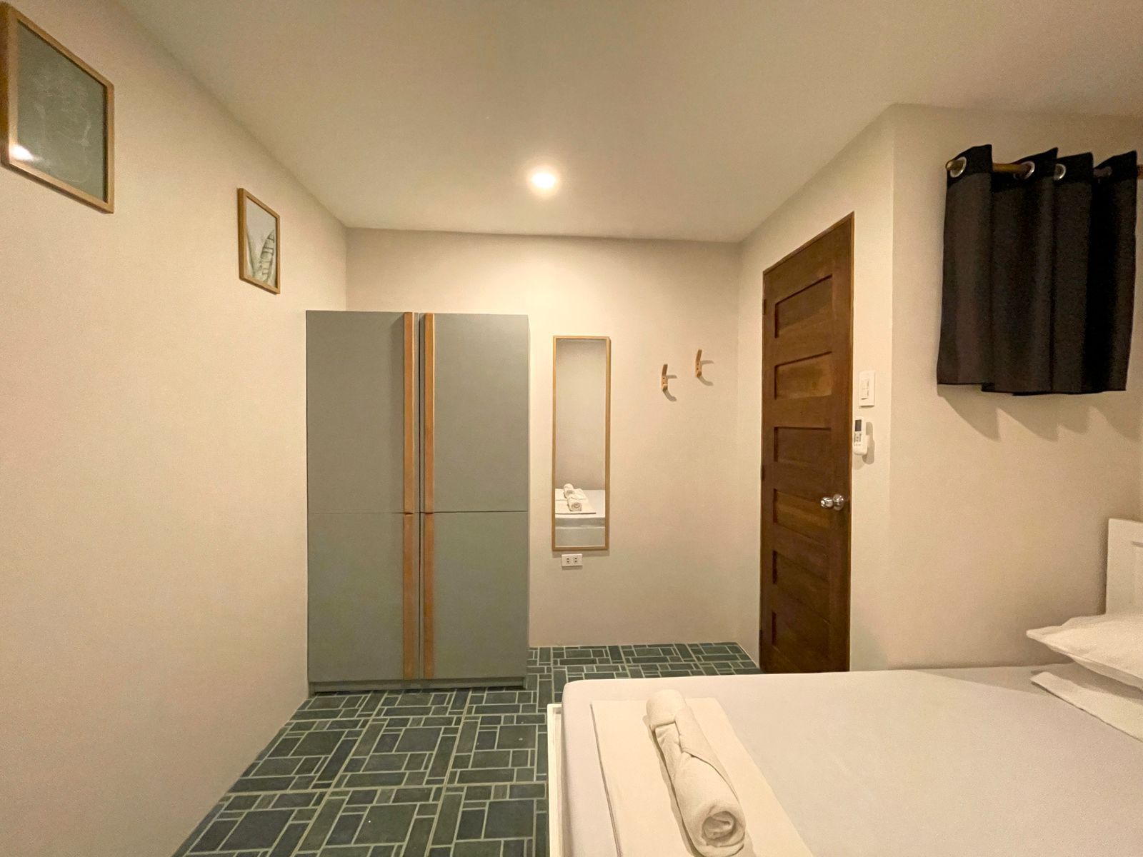 Bedroom with a bed, wardrobe, door, and patterned floor. Walls are light gray, wardrobe is gray.