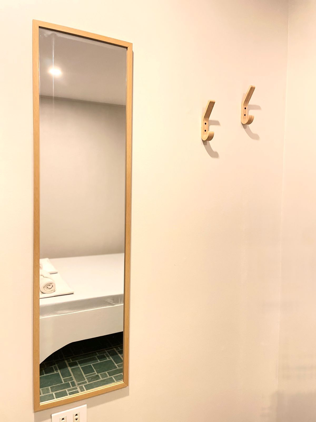 A long mirror reflects a bed, with two wall hooks beside it.