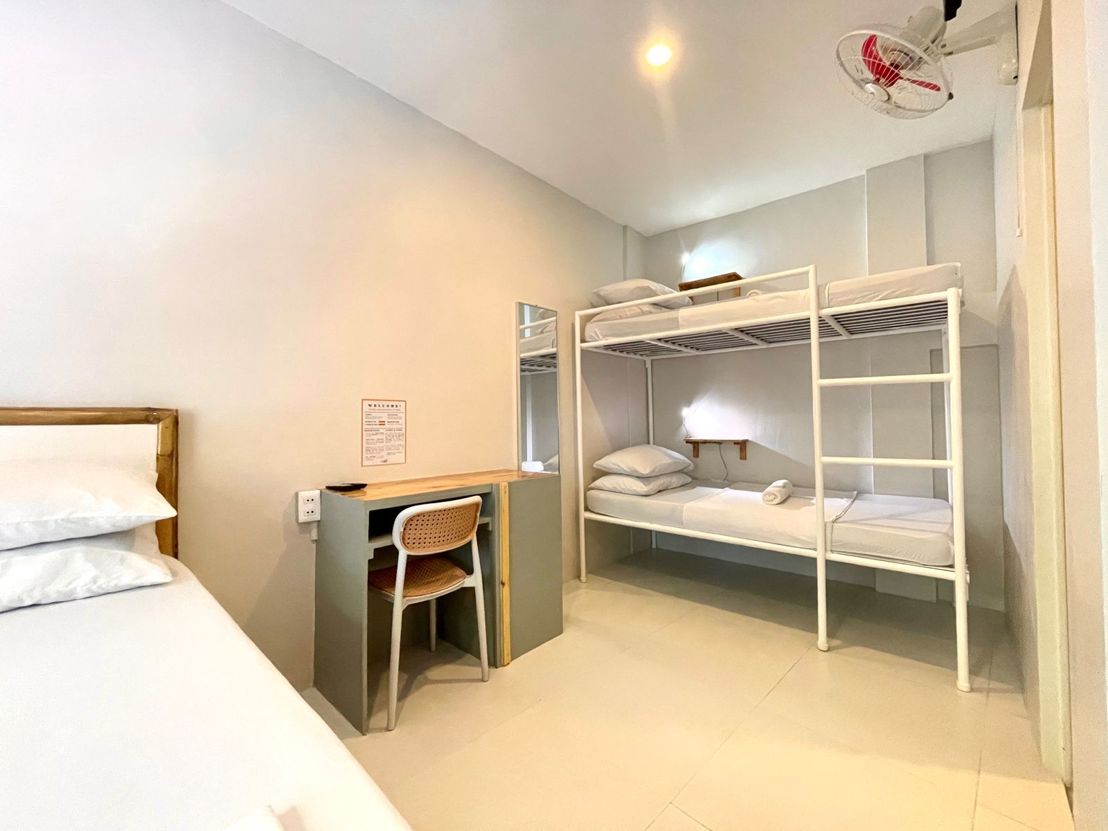 A hostel bedroom with bunk beds, a single bed, desk, and a ceiling fan.