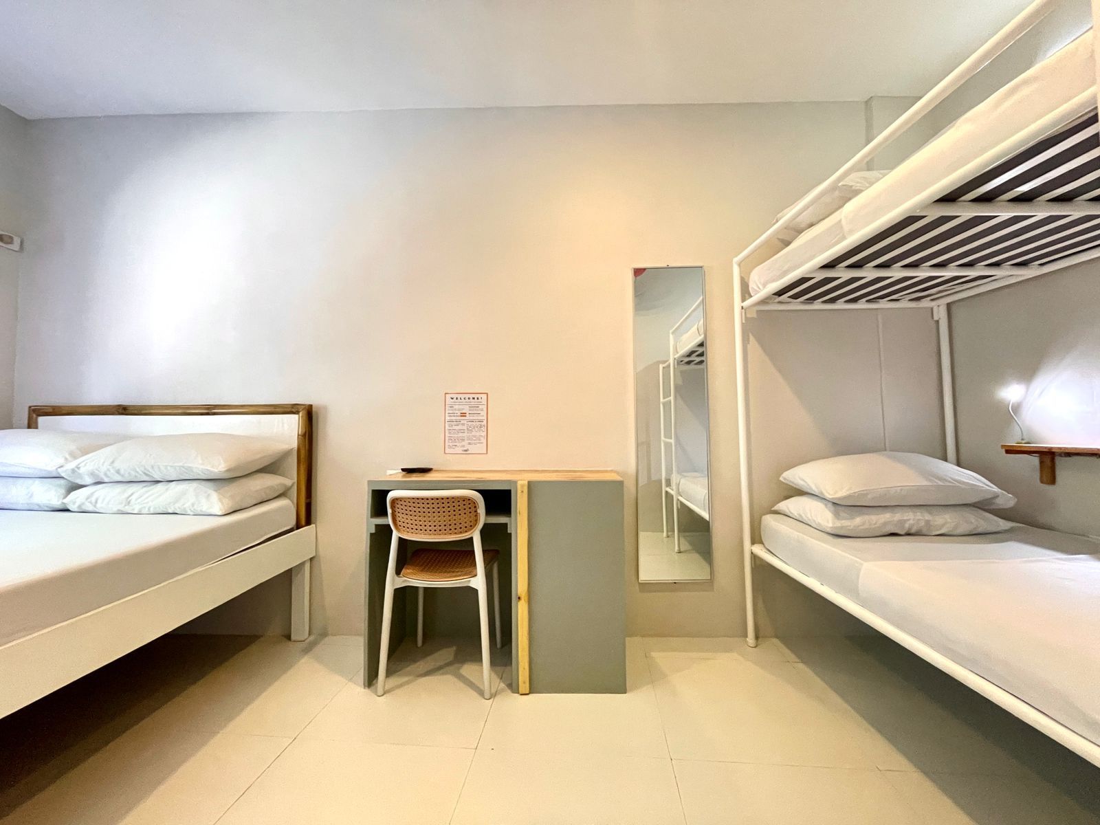 A dorm room with two bunk beds, a desk, and a mirror against a white-painted wall.