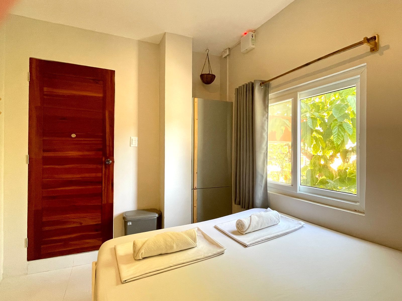 Bedroom with a bed, closed wooden door, window with curtains, and a small refrigerator.