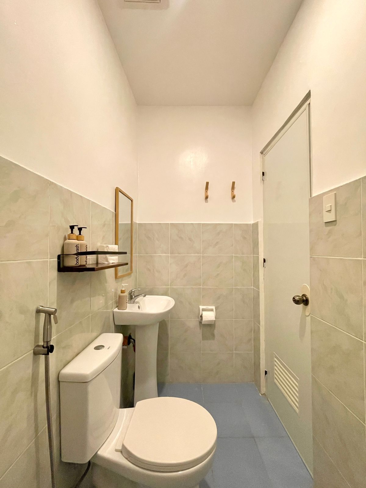 Small bathroom with blue floor, white toilet, pedestal sink, and gray tiled walls.