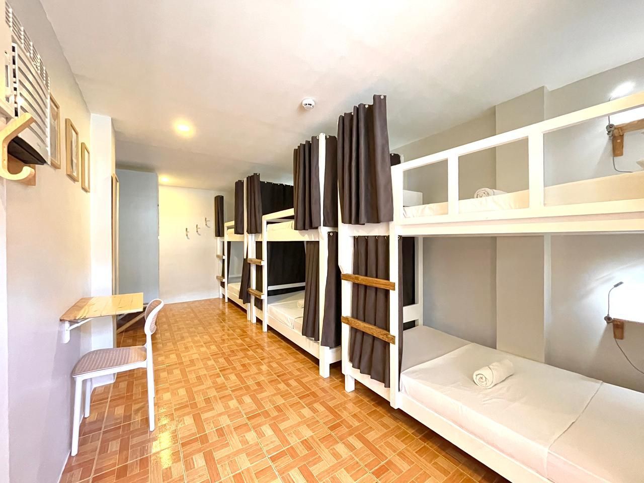 A hostel room with multiple bunk beds, brown curtains, and a desk.