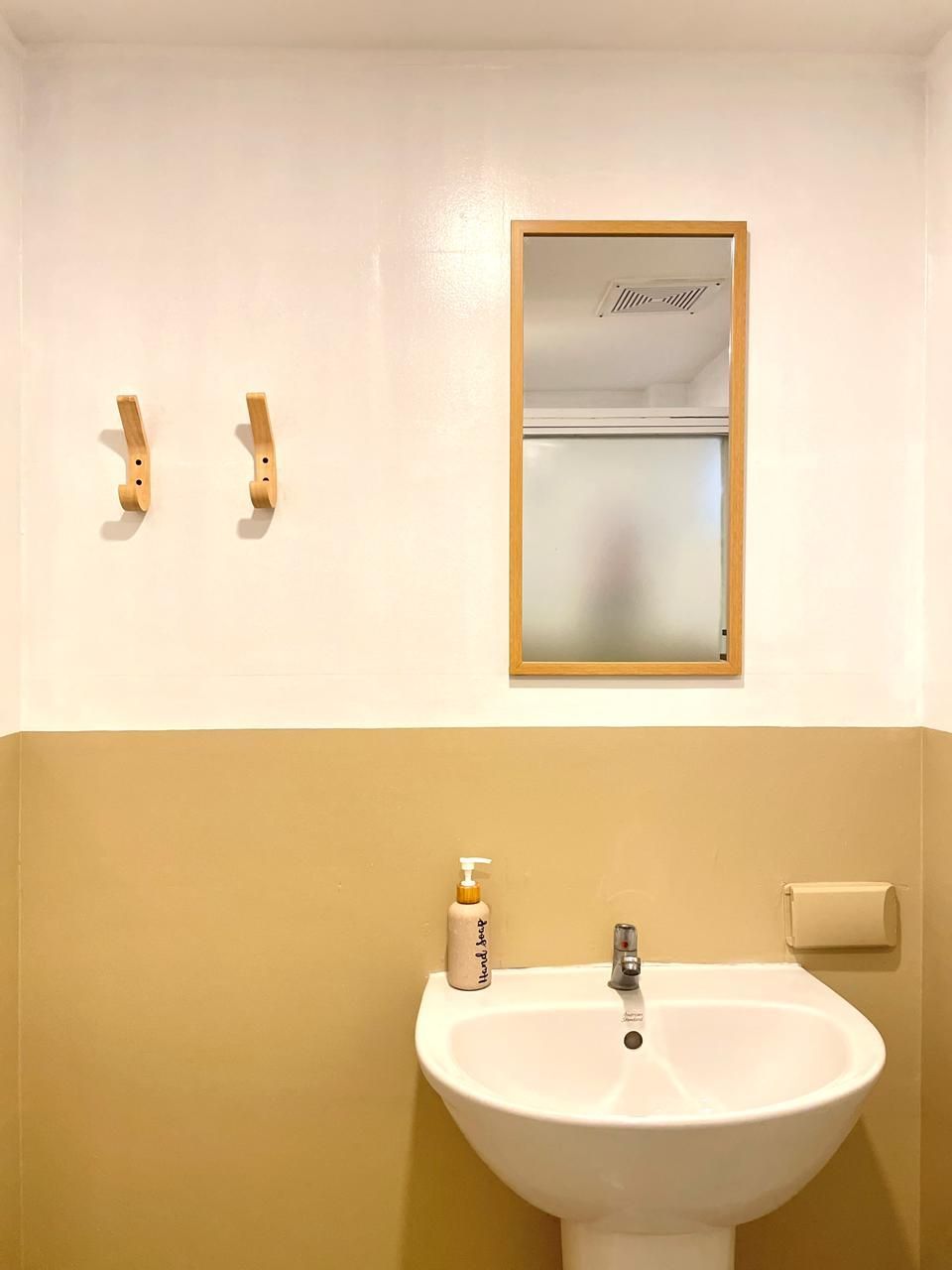 Bathroom with white sink, mirror, and two wooden hooks on a yellow and white wall.
