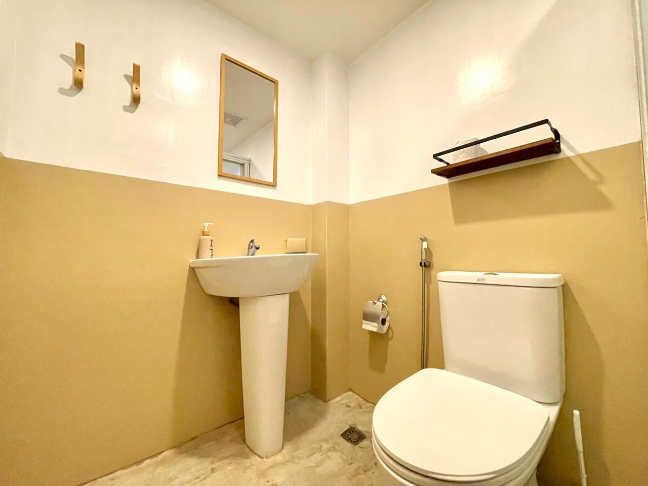 Small bathroom with pedestal sink, toilet, mirror, towel rack, and brass hooks; mustard and white walls.