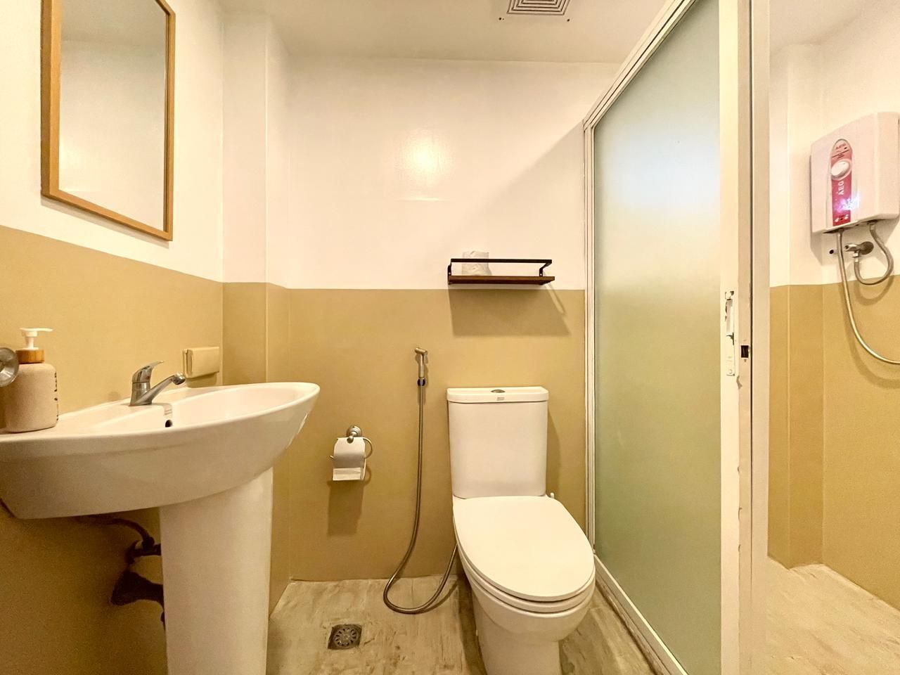 Bathroom with white and tan walls, pedestal sink, toilet, and glass shower door.
