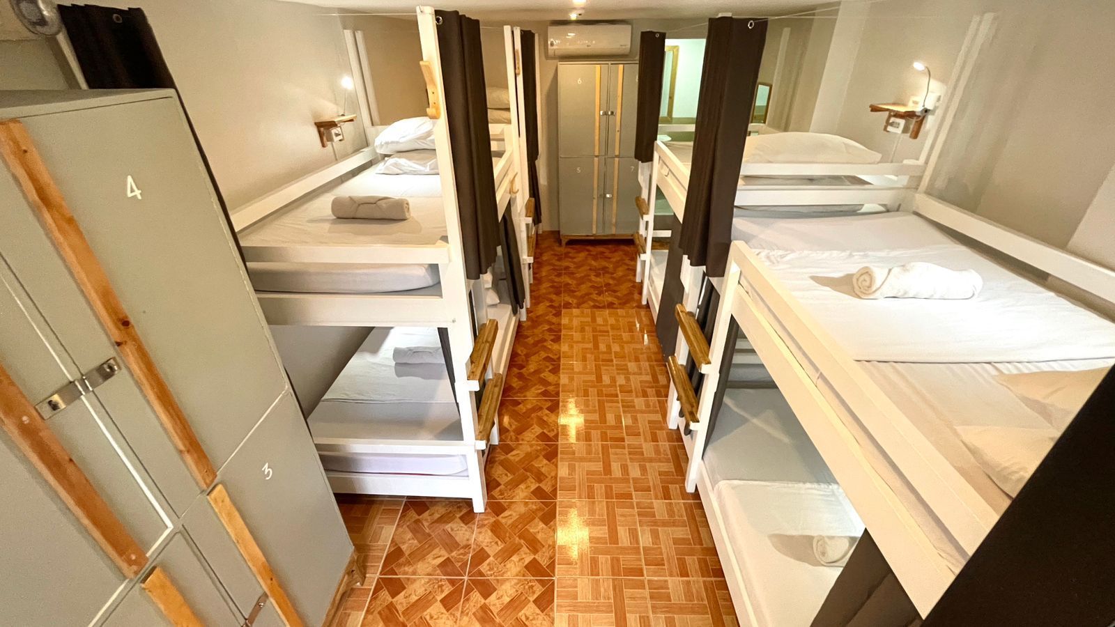 Bunk beds in a hostel room with neutral colors, lockers, and a central aisle.