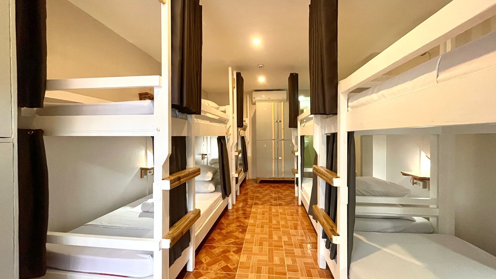 A hostel dormitory with multiple white bunk beds and privacy curtains.