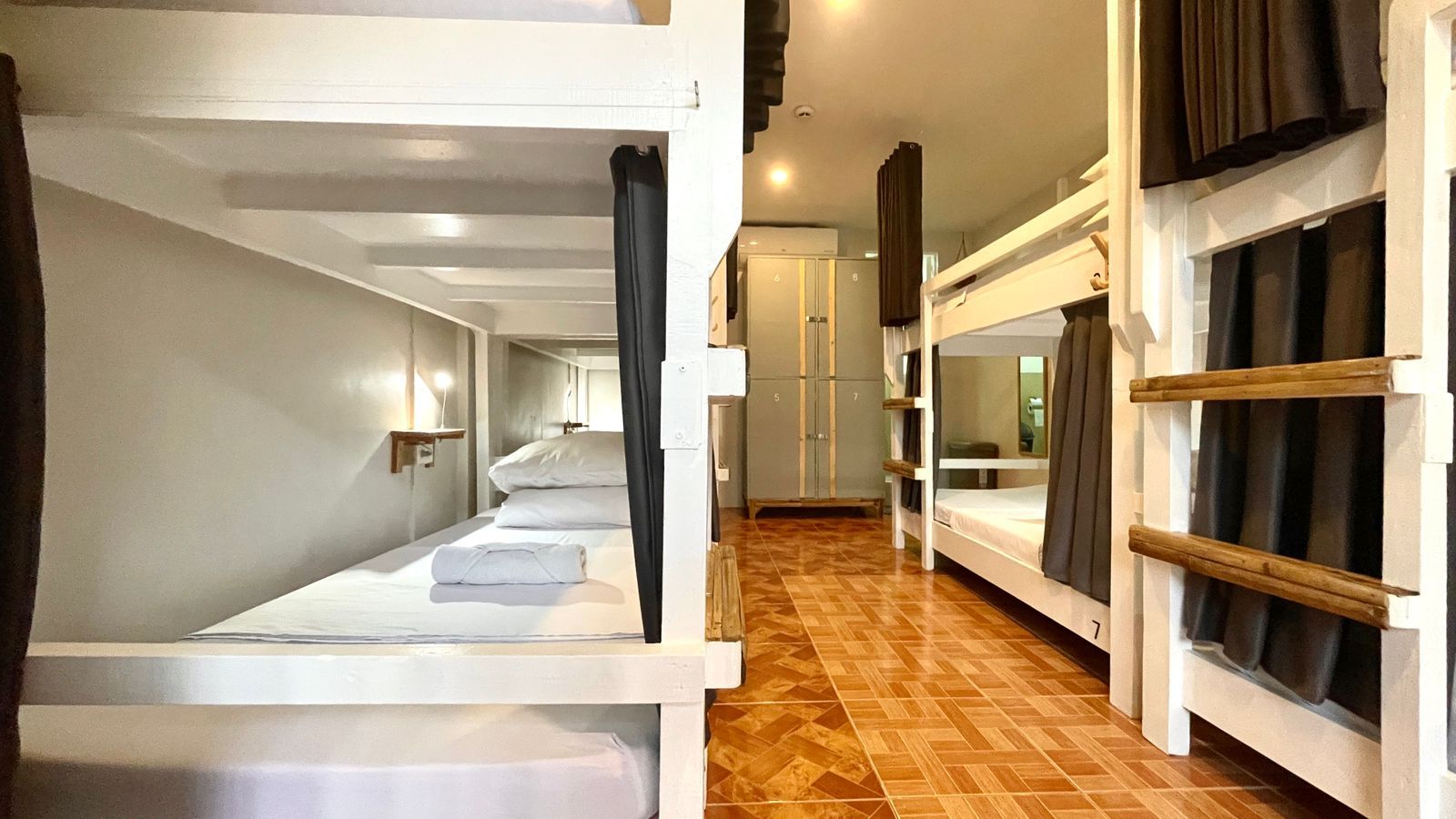 Bunk beds in a brightly lit hostel room, with gray curtains and tiled floor.