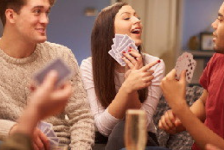 People playing cards; woman laughs, holding cards; others hold cards, indoors.