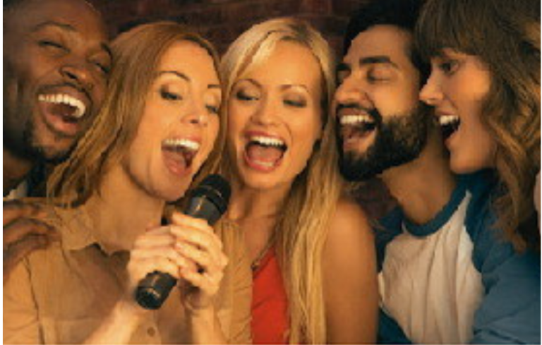 Five people singing into a microphone, laughing in a karaoke setting.