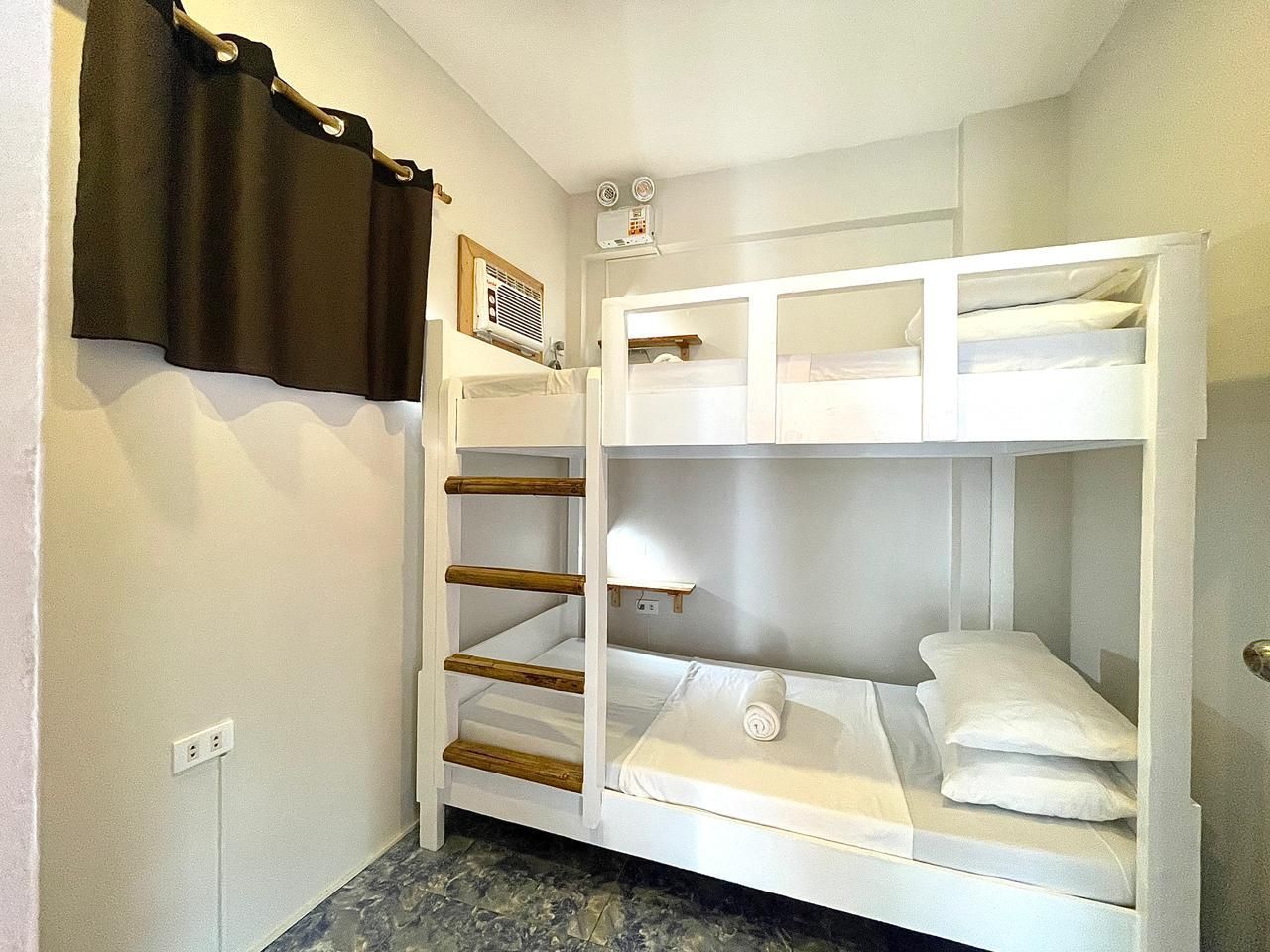 White bunk beds in a room with a brown curtain and neutral-colored walls.