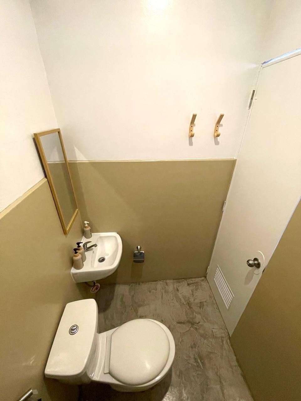 Small bathroom with toilet, sink, mirror, and neutral-toned walls.