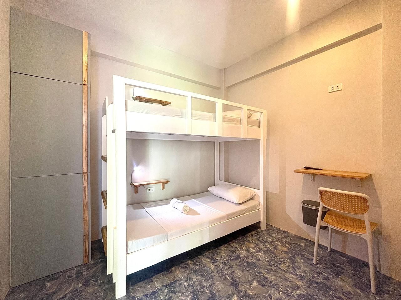 A small, white bunk bed in a simple room, with a cabinet and a small desk.
