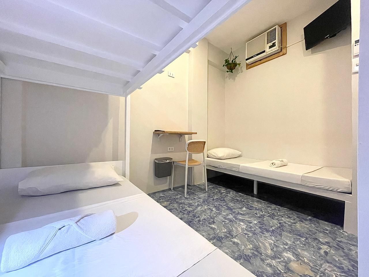 Bunk beds and a single bed in a small, white room. Air conditioner and TV on the wall. Blue patterned floor.