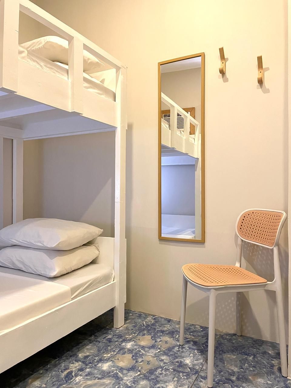 Bunk beds in a room with a mirror, chair, and hooks on the wall. The floor has a blue patterned design.