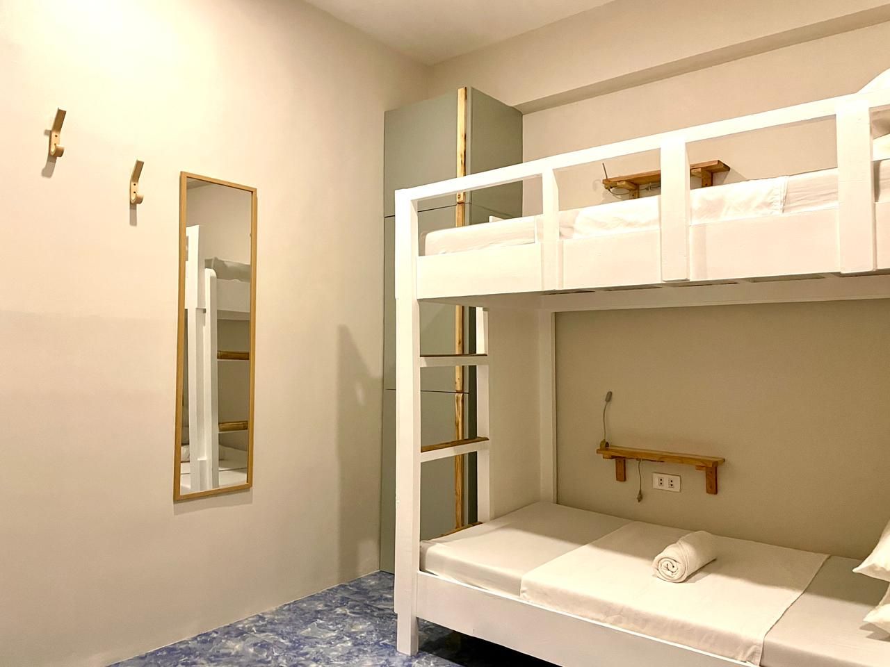 A small room with white bunk beds, a mirror, and a wall-mounted shelf.