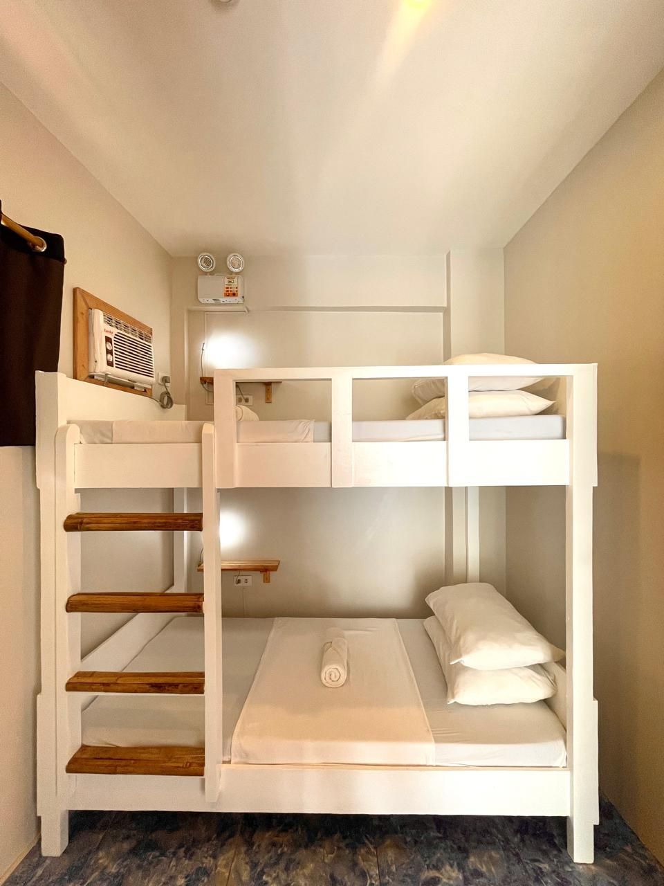 White bunk beds in a narrow room with wooden steps, white bedding, and a light-colored walls.