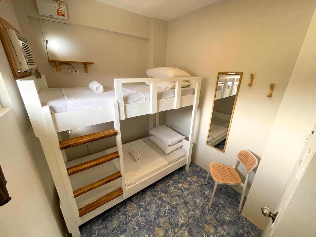 A small, white bunk bed in a room with blue patterned flooring, a mirror, and a chair.