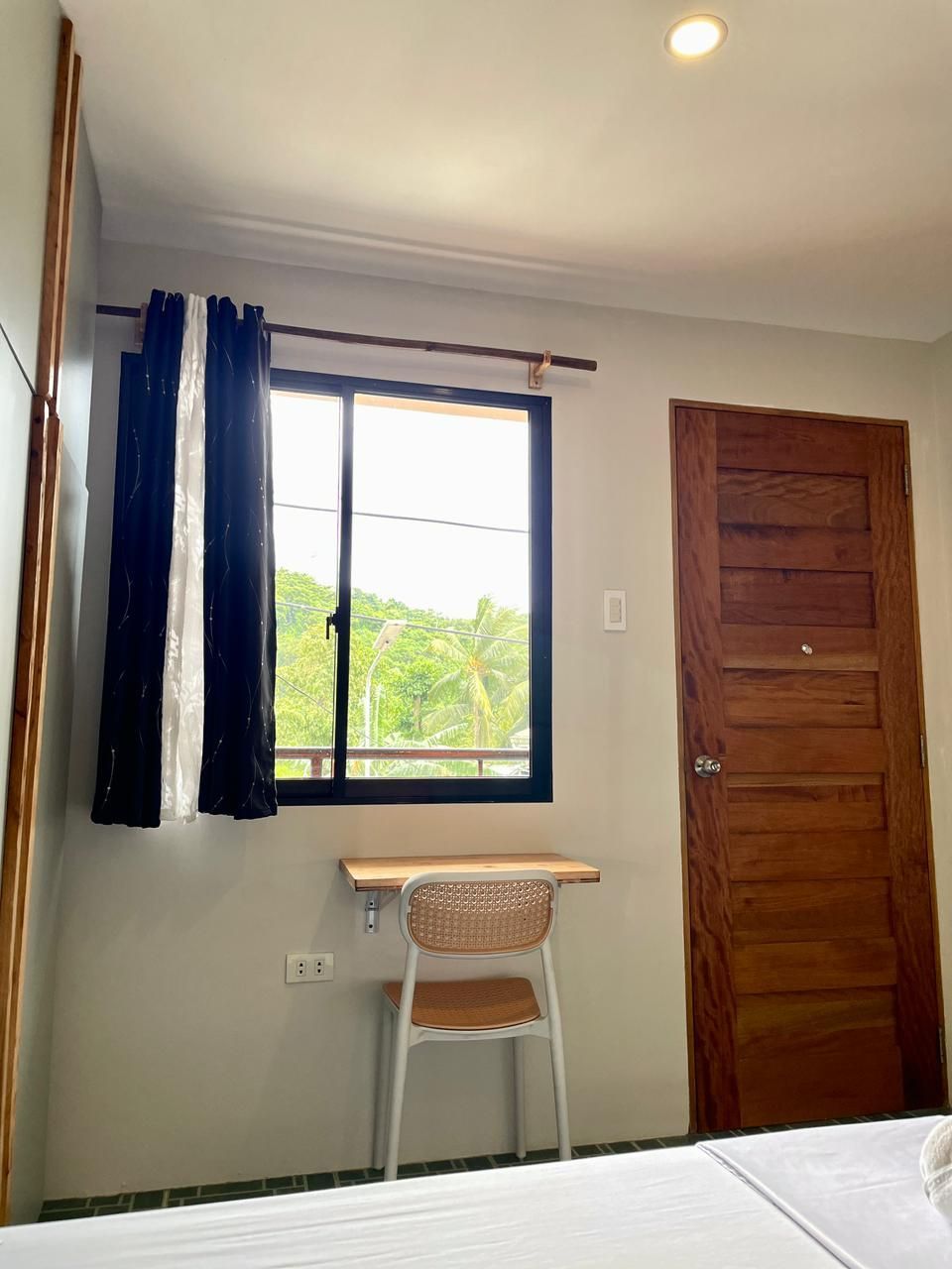 Room interior with window, desk, chair, and wooden door. Black and white curtains, white walls.