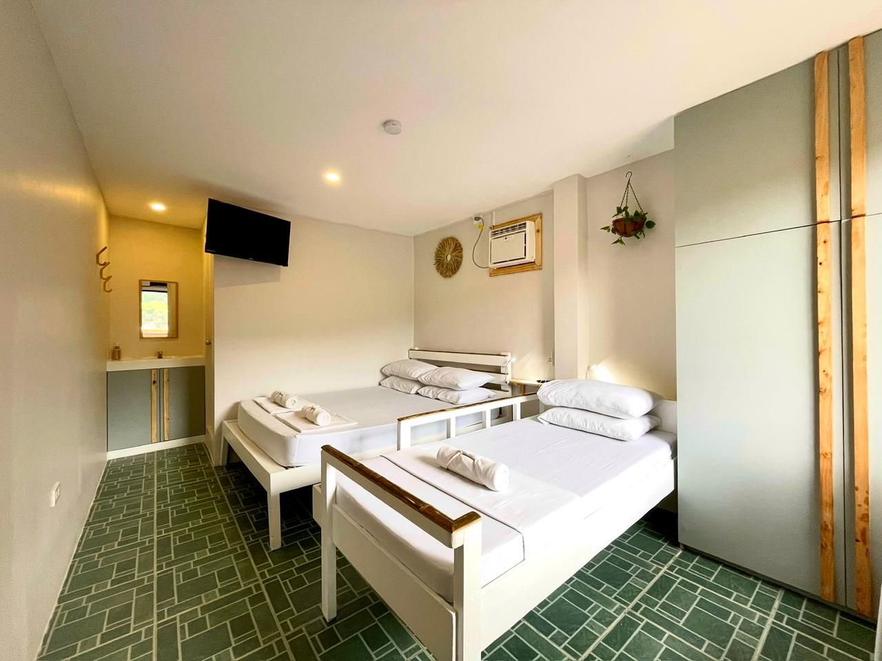 Bedroom with three beds, a TV, and a sink. Green tiled floor, light gray walls.