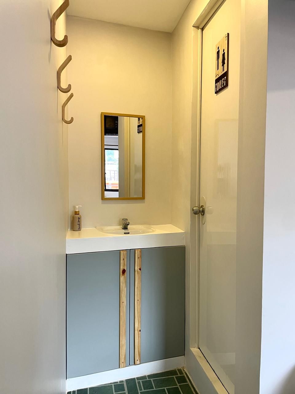Small bathroom with sink, mirror, and shower. Gray cabinet with wooden accents. Green tile floor.