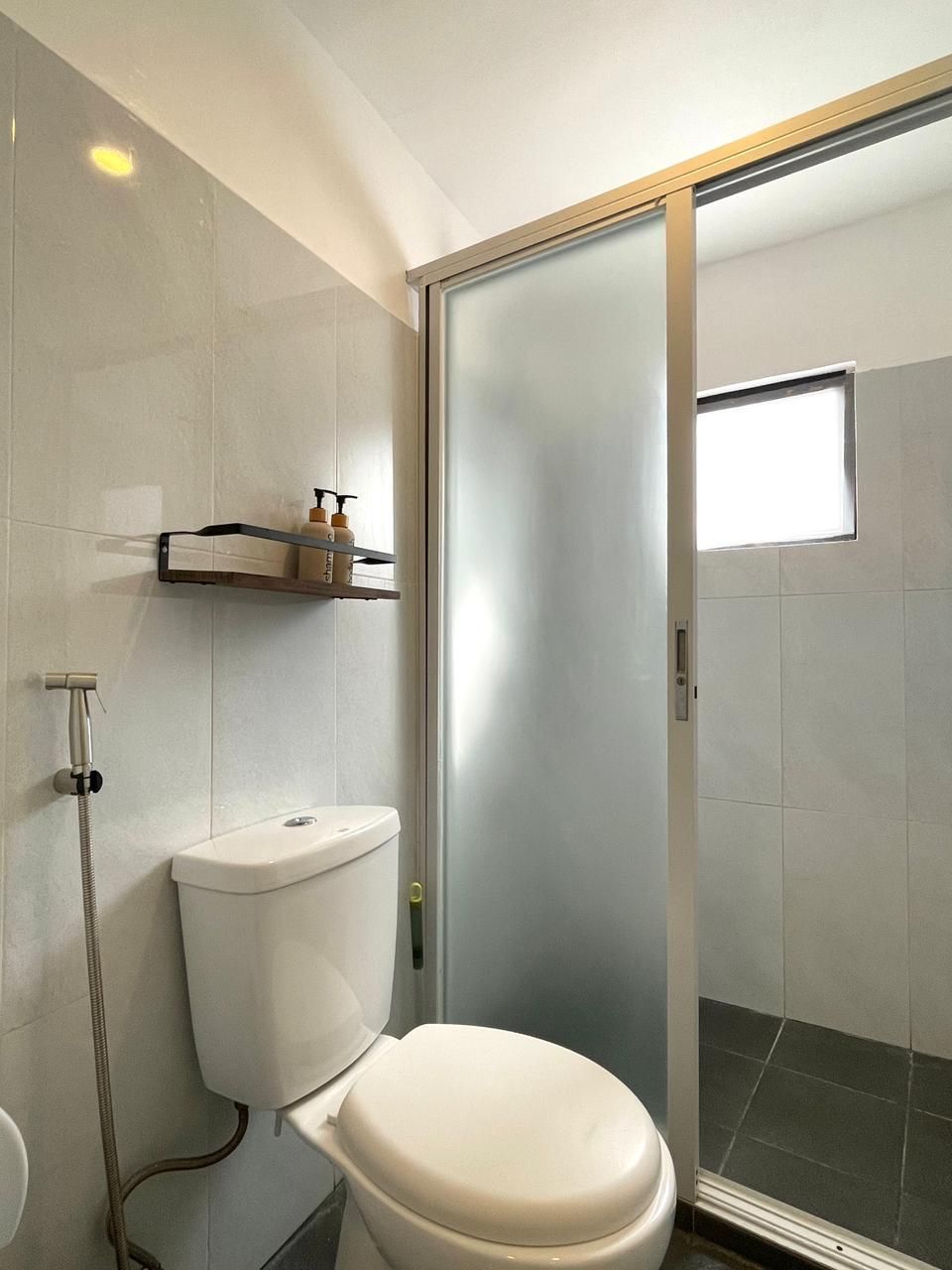 Bathroom with white toilet, frosted glass sliding door, shower, and gray tile walls.