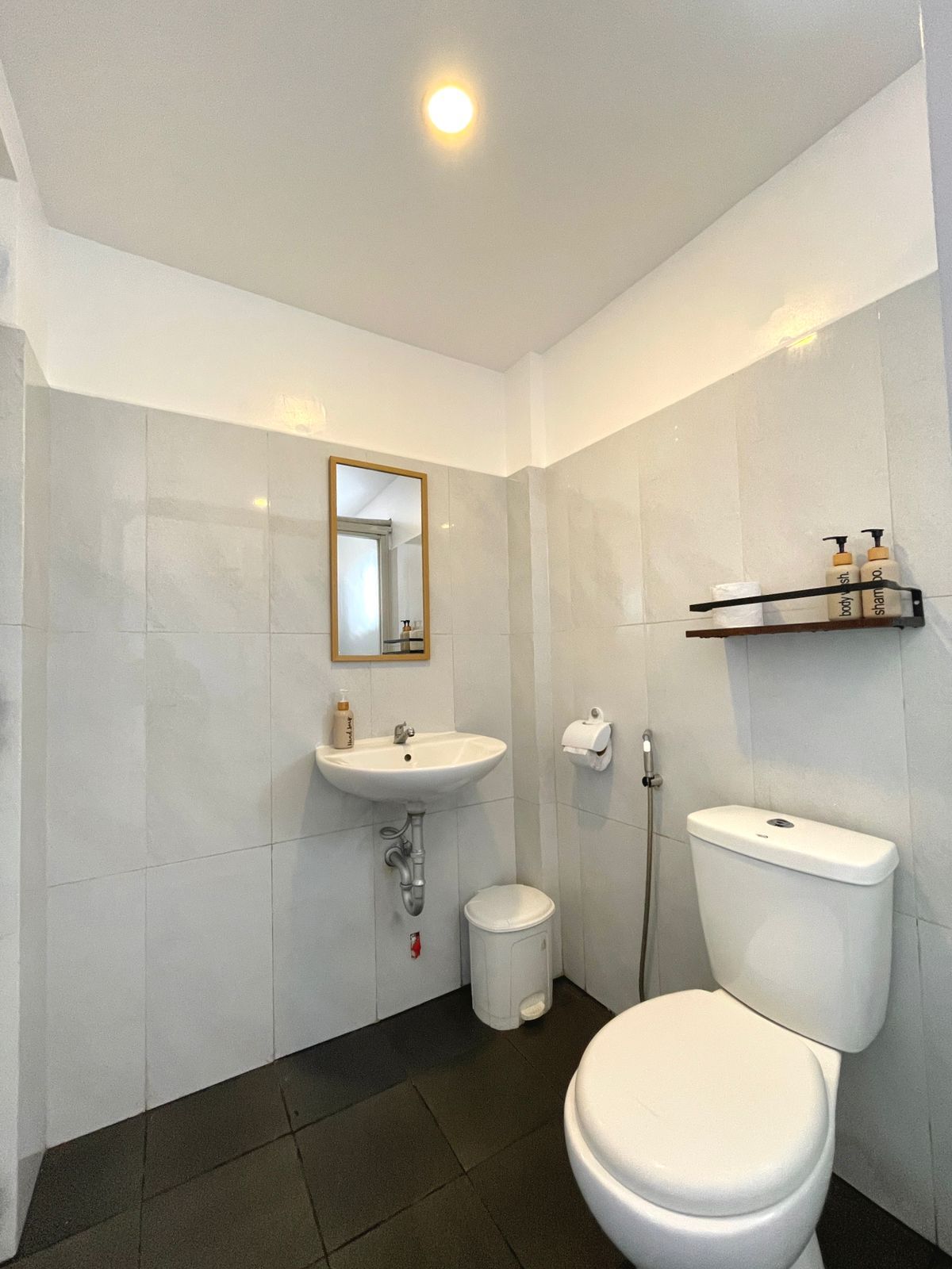 Bathroom with white tiled walls, toilet, sink, mirror, and black floor tiles.