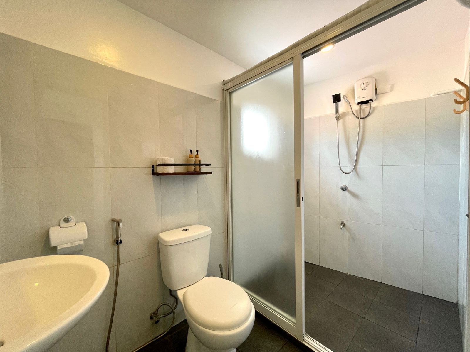 Bathroom with gray tiles, toilet, sink, and shower with sliding glass door.