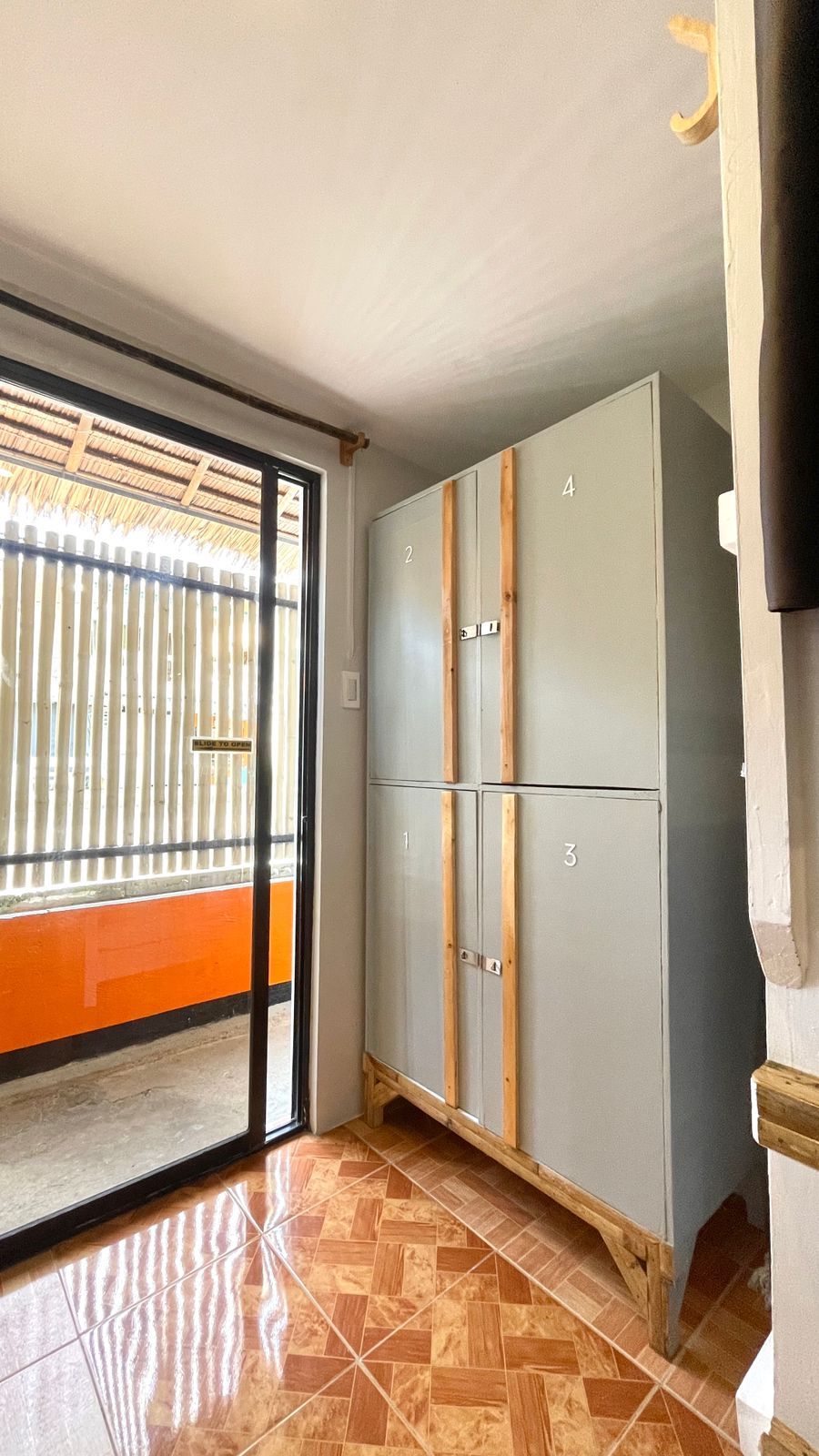 Gray storage cabinet inside a room with a sliding glass door and orange wall.